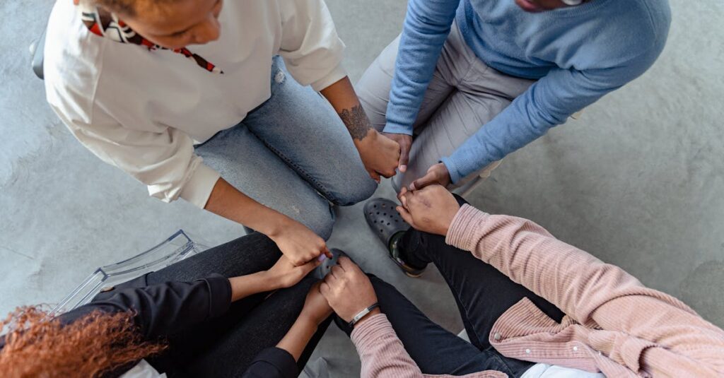 Four people sit in a circle holding hands, emphasizing unity and support in a therapy session.